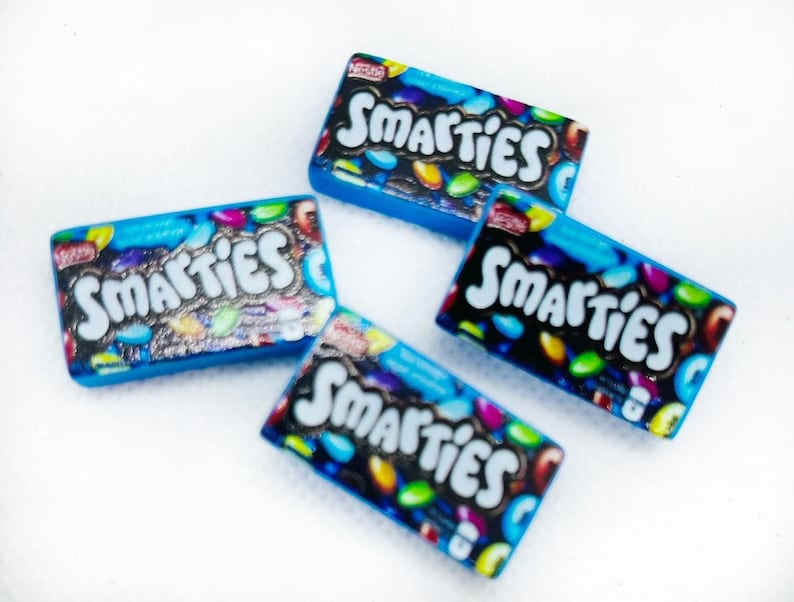 May include: Four miniature boxes of Smarties candy. The boxes are blue with a white background and feature the Smarties logo and colorful candies.