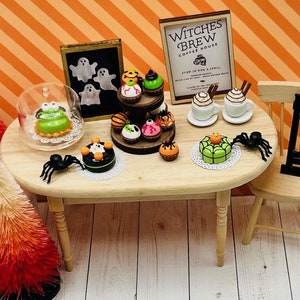 K&ouml;nnte beinhalten: Ein Miniatur-Halloween-Caf&eacute; mit einem Holztisch und St&uuml;hlen. Der Tisch ist mit verschiedenen Halloween-Cupcakes, Kuchen und Kaffee dekoriert. Das Schild &uuml;ber dem Caf&eacute; lautet "Witches Brew Coffee House".