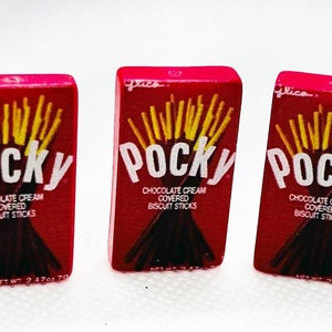 May include: Three red boxes of Pocky chocolate cream covered biscuit sticks. The boxes are stacked side by side and have the Pocky logo and product description printed on them.