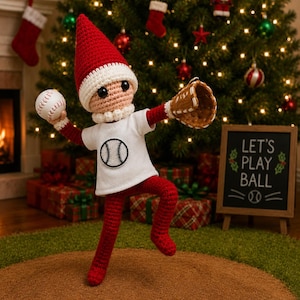 May include: A crocheted elf doll wearing a red pointed hat with a white trim, a white t-shirt with a baseball graphic, and red pants. The doll holds a white baseball in one hand and wears a brown baseball glove on the other, posed as a pitcher.