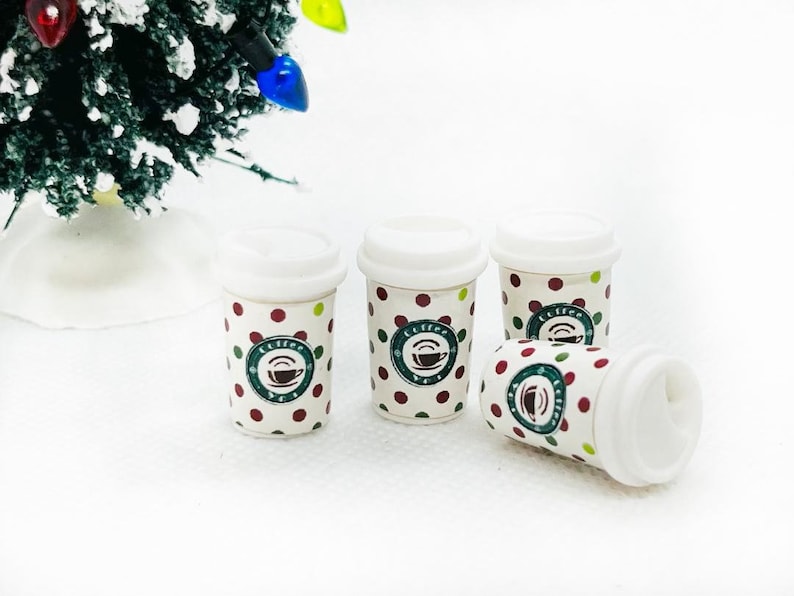 K&ouml;nnte beinhalten: Vier wei&szlig;e Miniatur-To-Go-Becher mit roten und gr&uuml;nen Punkten und einem gr&uuml;nen Kaffeetassen-Logo. Die Becher stehen auf einer wei&szlig;en Oberfl&auml;che.