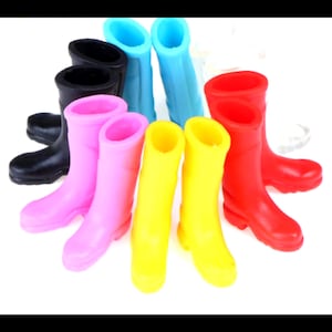 Könnte beinhalten: Ein Set mit neun bunten Regen-Stiefeln für Puppen. Die Stiefel sind in verschiedenen Farben, darunter Schwarz, Blau, Rosa, Gelb und Rot.