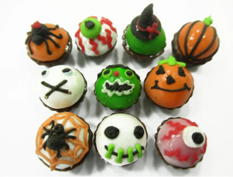K&ouml;nnte beinhalten: Eine Sammlung von zehn Halloween-Cupcakes, die mit verschiedenen gruseligen Designs verziert sind, darunter eine Spinne, ein K&uuml;rbis, ein Geist und ein Auge. Die Cupcakes sind alle in verschiedenen Farben glasiert, darunter Orange, Gr&uuml;n, Wei&szlig; und Pink.