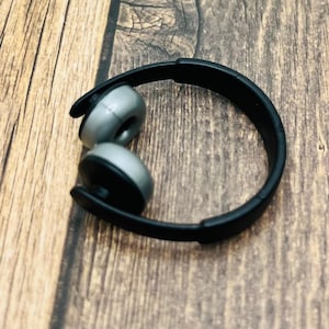Könnte beinhalten: Schwarzer und silberner Kopfhörer mit gebogenem Bügel. Die Ohrmuscheln sind silberfarben mit schwarzen Akzenten. Der Kopfhörer liegt auf einer Holzoberfläche.