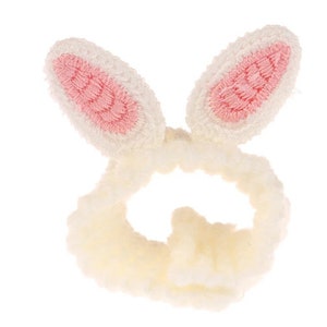 May include: A white fuzzy headband with pink bunny ears. The headband is made of soft, fluffy material and is designed to hold back hair.