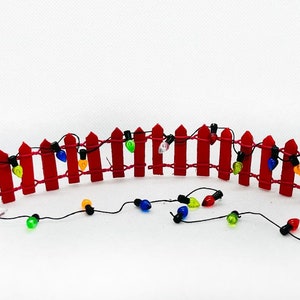 May include: A red picket fence with a string of colorful lights draped over it. The lights are strung along the fence and are hanging down on either side.