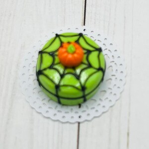 K&ouml;nnte beinhalten: Ein gr&uuml;ner und schwarzer Schokoladenkeks mit Spinnennetz-Muster und einem orangefarbenen K&uuml;rbis darauf.