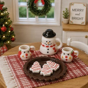May include: A miniature ceramic tea set featuring a snowman-shaped teapot with a black hat, two small mugs with red and yellow accents, and a brown scalloped plate holding three white Christmas tree-shaped cookies with red icing stripes.
