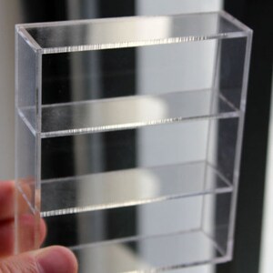 K&ouml;nnte beinhalten: Ein klares Acryl-Regal mit drei Regalb&ouml;den. Die Regalb&ouml;den sind aus klarem Acryl und werden von klaren Acryl-Haltern getragen.