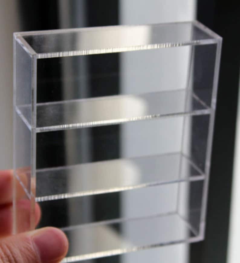 K&ouml;nnte beinhalten: Ein klares Acryl-Regal mit drei Regalb&ouml;den. Die Regalb&ouml;den sind aus klarem Acryl und werden von klaren Acryl-Haltern getragen.