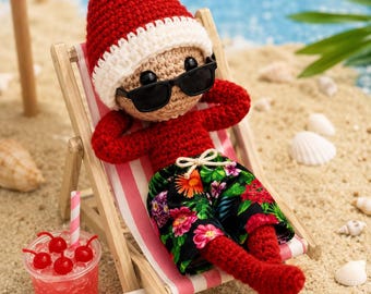 May include: A crocheted doll with a red pointed hat, black sunglasses, and a red long-sleeved shirt, wearing black shorts with a colorful floral print. The doll rests in a miniature wooden beach chair next to a red drink and a sign reading Beach Day!