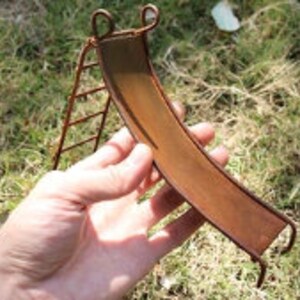 May include: A miniature rusty metal slide with a ladder, ideal for a fairy garden or miniature scene.