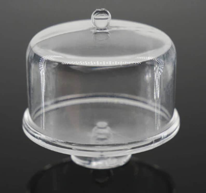 K&ouml;nnte beinhalten: Eine transparente Kuchenhaube aus Kunststoff mit einem runden Sockel und einem Knopf oben. Die Haube ist dazu bestimmt, Kuchen oder andere Desserts abzudecken und zu sch&uuml;tzen.