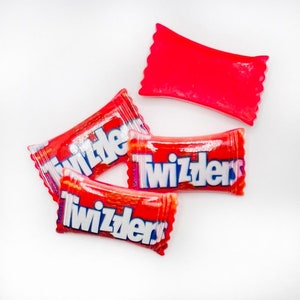 May include: Four red Twizzlers candy wrappers, three of which are lying flat on a white surface. The wrappers have the word "Twizzlers" printed in white letters with blue outlines.