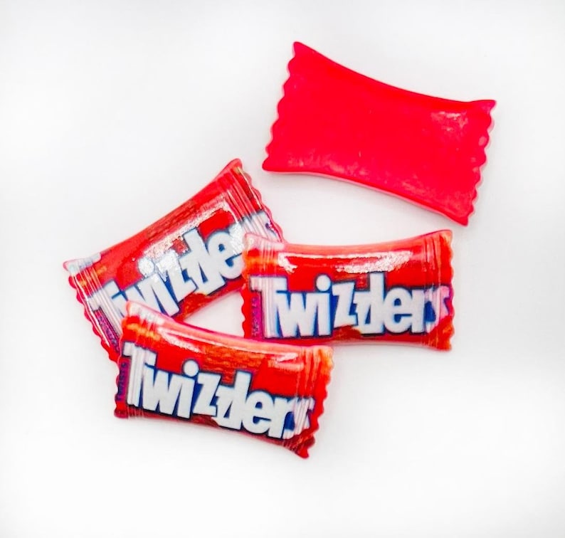 May include: Four red Twizzlers candy wrappers, three of which are lying flat on a white surface. The wrappers have the word "Twizzlers" printed in white letters with blue outlines.