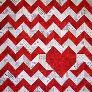 May include: A red and white chevron quilt with a large red heart in the center. The heart is made of smaller red fabric squares with a floral pattern. The quilt is made of a variety of fabrics with a white background and black designs.