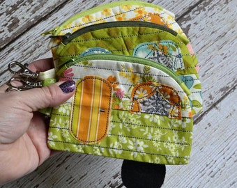 May include: A set of four green, yellow, and white fabric coin purses with a camper van design. The purses have zippers and are lined with a floral print.