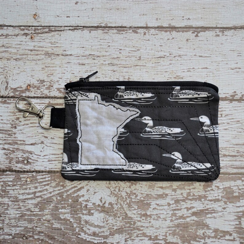 May include: A black zippered pouch with a white outline of the state of Minnesota and a pattern of white loon birds on a black background.