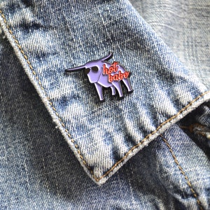 Puede incluir: Pin de esmalte morado de un toro con el texto "hot babe" en letras rojas. El pin est&aacute; en una chaqueta vaquera azul.