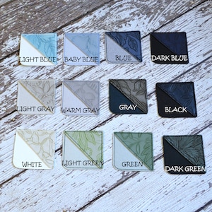 May include: Twelve fabric bookmark samples in various colors, including light blue, baby blue, blue, dark blue, light gray, warm gray, gray, black, white, light green, green, and dark green. Each bookmark has a floral design.