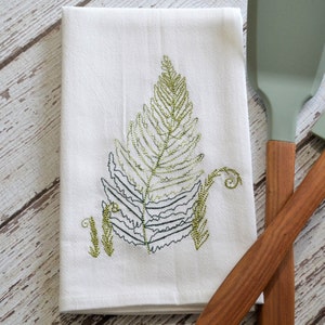 May include: White kitchen towel with an embroidered green fern design.