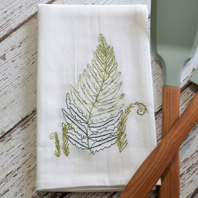 May include: White kitchen towel with an embroidered green fern design.