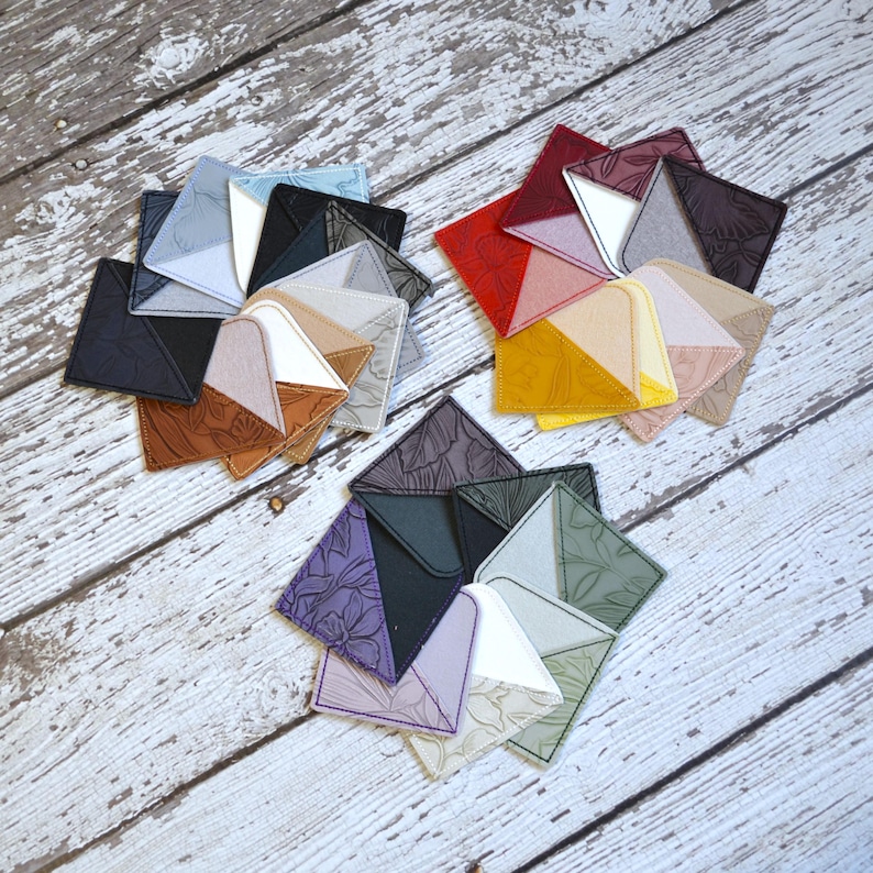 May include: Assortment of fabric squares in various colors and patterns, including black, red, yellow, green, purple, and brown. The squares are arranged in a circular pattern on a white wooden surface.
