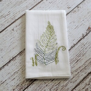 May include: White kitchen towel with an embroidered green fern design.