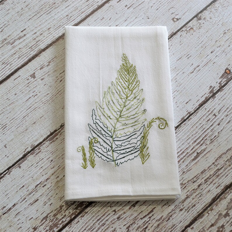 May include: White kitchen towel with an embroidered green fern design.