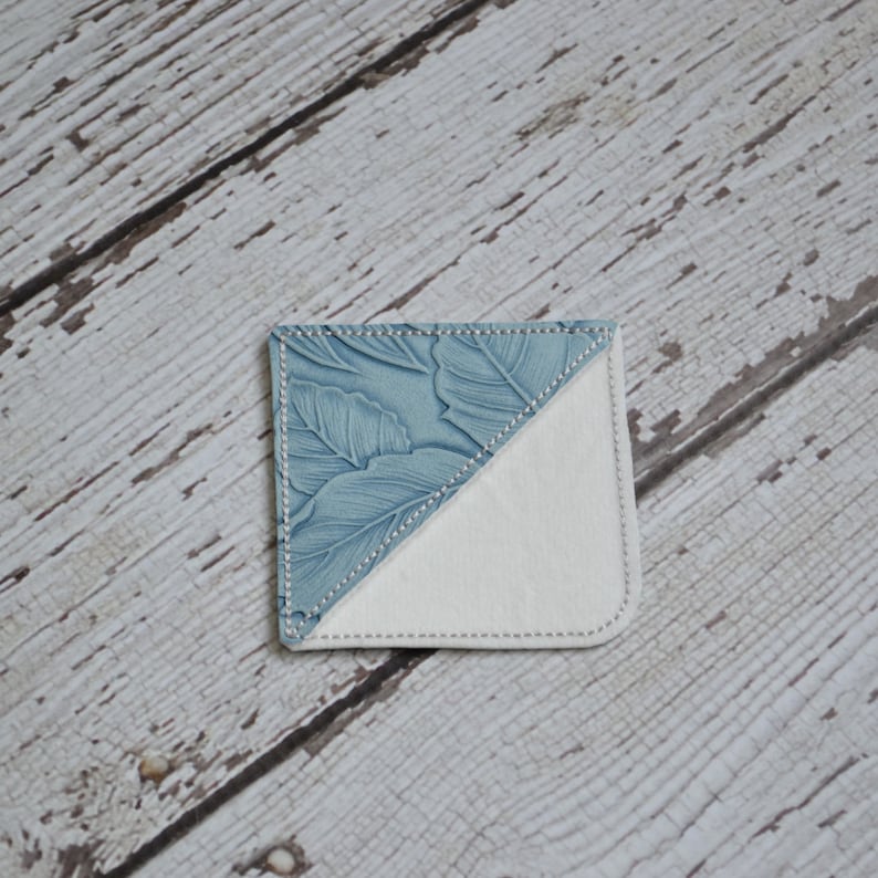 May include: A blue and white fabric bookmark with a floral pattern. The bookmark is folded in half, with the blue side facing up and the white side facing down.