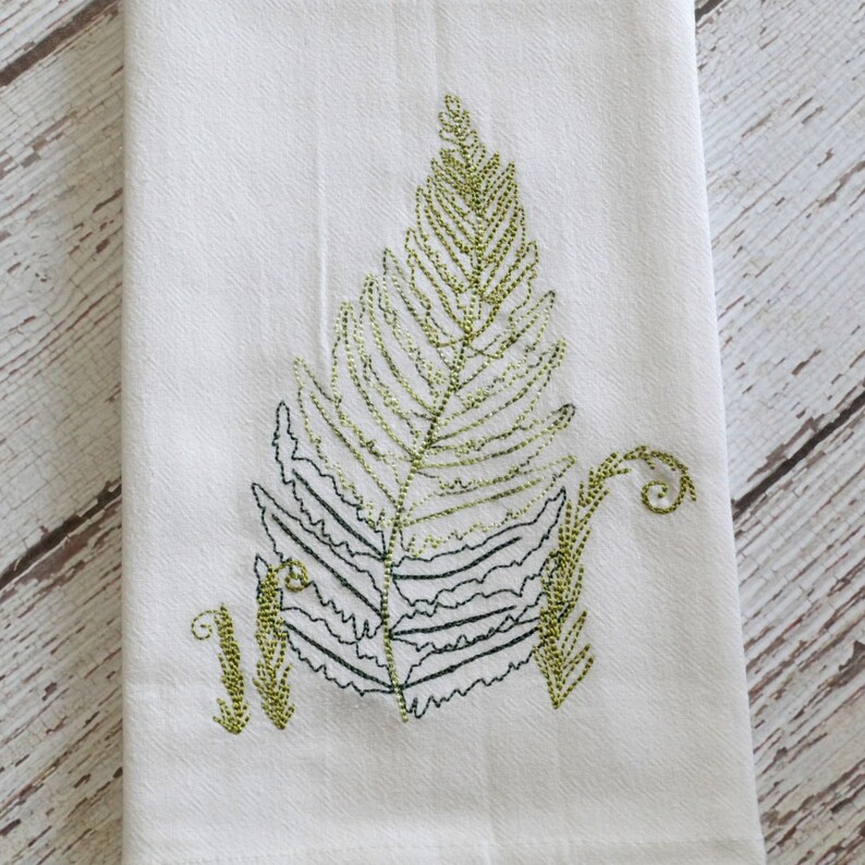 May include: A white kitchen towel with an embroidered green fern design.