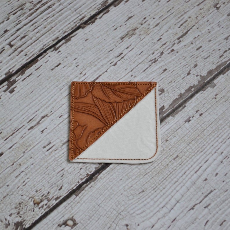 May include: A brown leather bookmark with a floral design on one side and a white fabric on the other side.