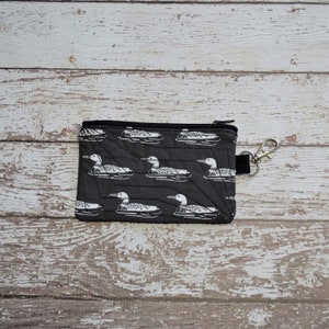 May include: A black zippered pouch with a white loon pattern. The pouch has a black zipper and a silver key ring.