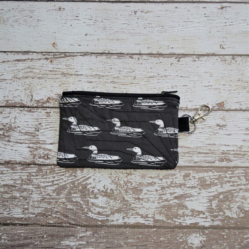 May include: A black zippered pouch with a white loon pattern. The pouch has a black zipper and a silver key ring.