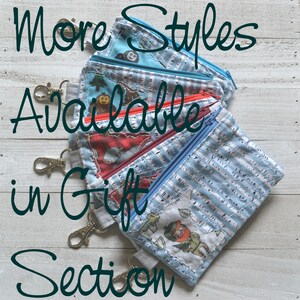 May include: A stack of five small zippered pouches with different colorful patterns and designs. The pouches have key rings attached. The text "More Styles Available in Gift Section" is written in black cursive letters on a white background.
