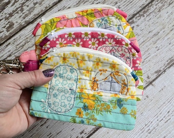 May include: Three colorful zippered pouches with floral patterns and a camper design. The pouches are made of fabric and have a zipper closure.
