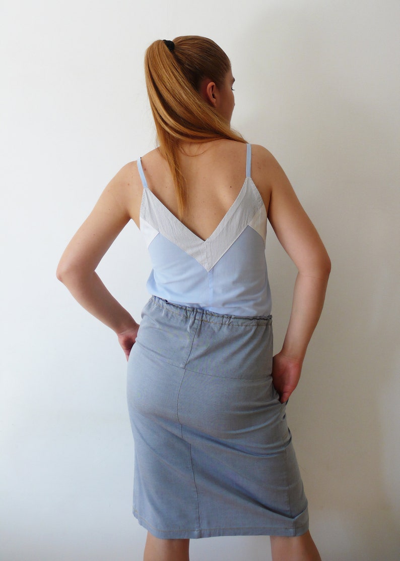 May include: A light blue sleeveless top with a white and light blue striped design. The top has a V-neckline and is paired with a light blue denim skirt.