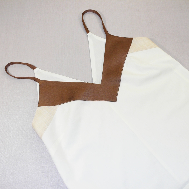 May include: A white sleeveless top with a brown leather trim around the neckline. The top has a V-neck and a relaxed fit.
