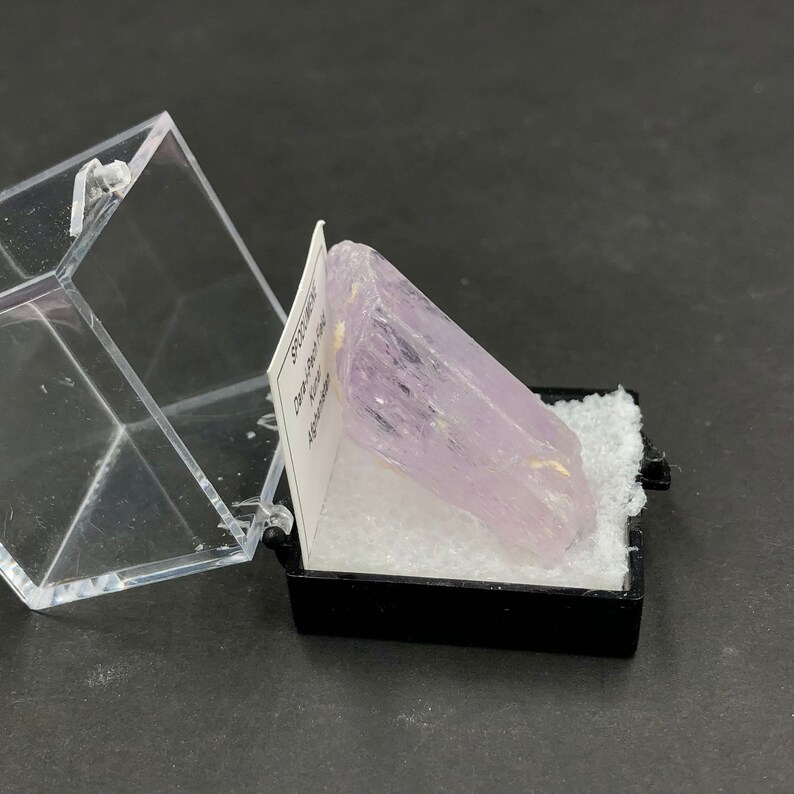 May include: A pale lavender crystal specimen in a small, clear plastic display box with a white label that reads "Spodumene,  Kunzite,  Afghanistan".