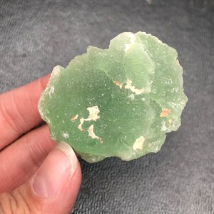 May include: A green fluorite crystal with white inclusions. The crystal has a rough, natural texture.
