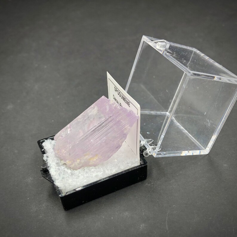 May include: A pink and white, translucent,  spodumene crystal in a small, black display box with a white label that reads "SPODUMENE".