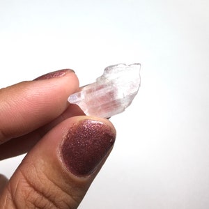 Puede incluir: Un peque&ntilde;o cristal transparente y transl&uacute;cido con una superficie estriada. El cristal se sostiene en una mano con esmalte de u&ntilde;as marr&oacute;n oscuro.