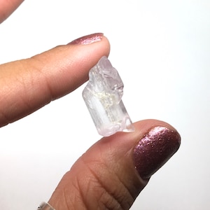 Puede incluir: Un cristal transparente y transl&uacute;cido con un tono rosado. El cristal tiene una forma puntiaguda y mide aproximadamente 2,5 cm de largo.