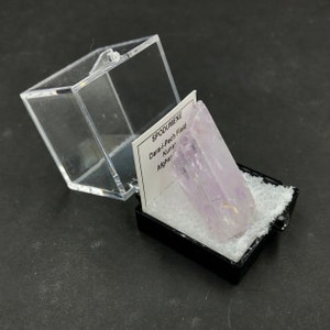 May include: A small, clear plastic box with a lid contains a light purple crystal labeled "SPODUMENE Dara-i-Pech Field Kunar Afghan"