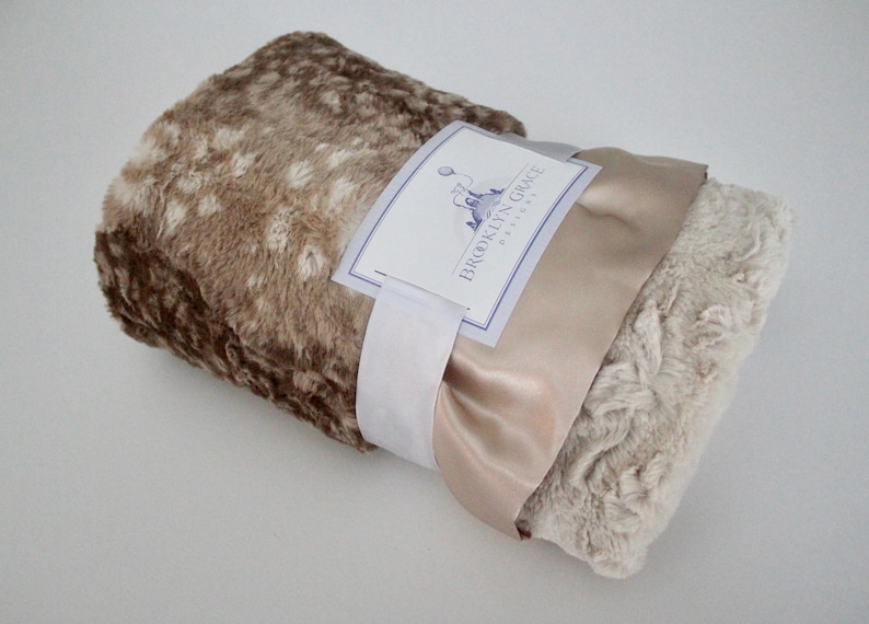 May include: A brown and beige faux fur throw blanket with a satin ribbon tied around it. The blanket is rolled up and the label "BROOKLYN GRACE DESIGNS" is visible.