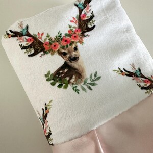 May include: A white stocking with a pink cuff features a printed design of a deer with a floral crown. The deer has brown antlers and a brown and white spotted body.