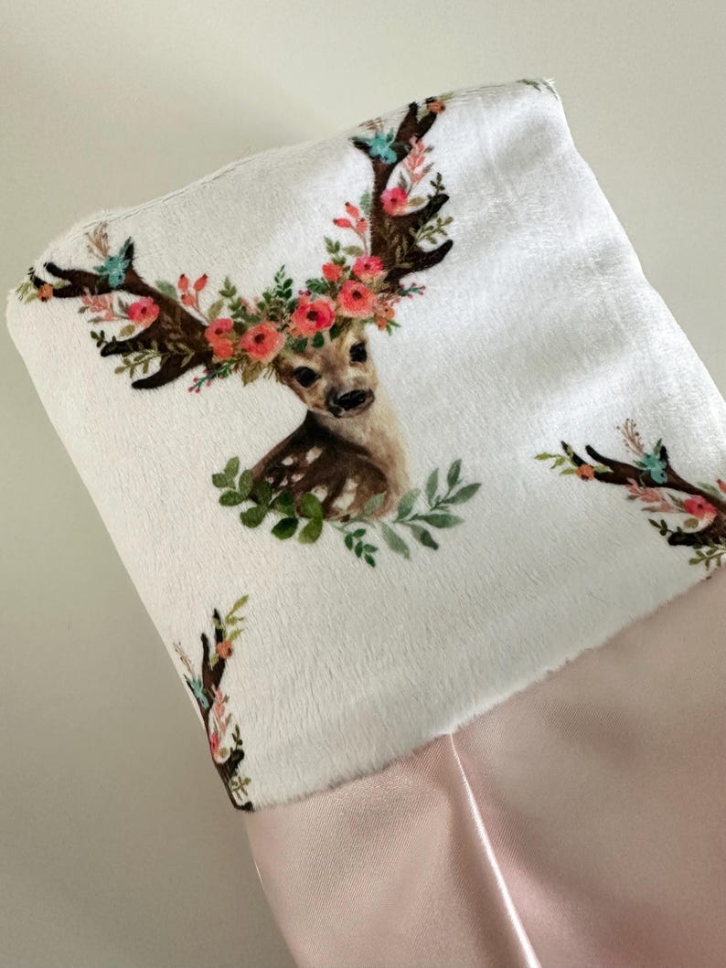 May include: A white stocking with a pink cuff features a printed design of a deer with a floral crown. The deer has brown antlers and a brown and white spotted body.