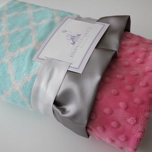 May include: A soft, pink and blue baby blanket with a white satin ribbon and a tag that reads "Brooklyn Grace Designs".