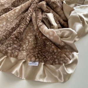 May include: A soft, brown and white faux fur baby blanket with a satin trim. The blanket has a subtle deer print pattern and a tag that reads "Everly Grace Designs".