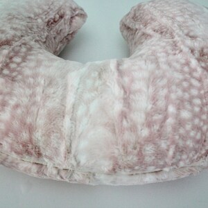 May include: A pink and white faux fur U-shaped pregnancy pillow with a white label that says "Dreamin' Grace Designs".